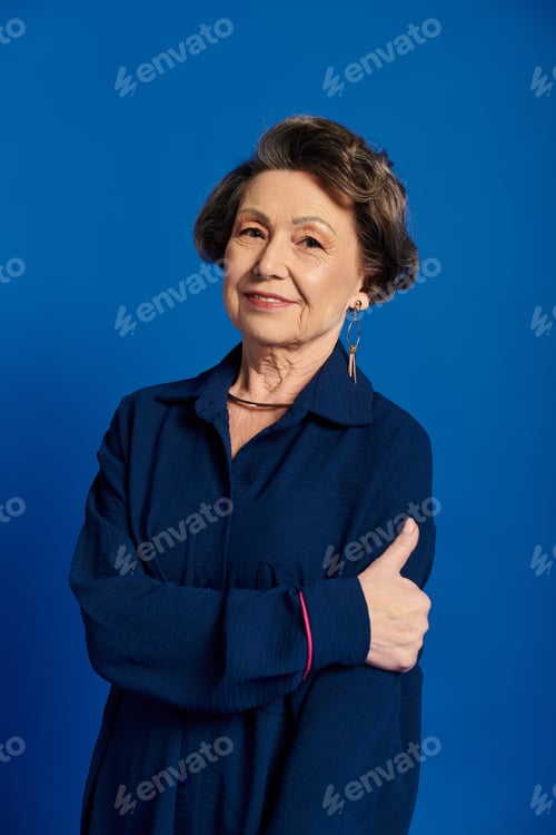 Preview: A confident woman in her 60s shows off her stylish fashion against a bright blue backdrop.