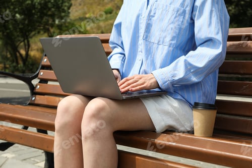 Preview: The girl works on a laptop while sitting on a bench