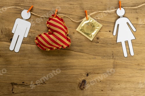 Preview: Close-up of paper couple with heart shape and condom hanging on clothesline over wooden table