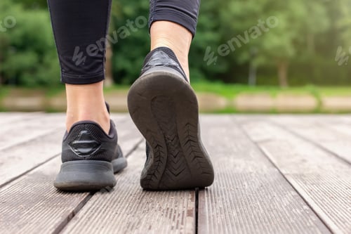 Preview: Close-up of women's legs in black sneakers walking on a wooden deck