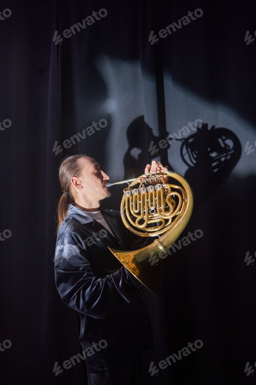 Preview: Musician Playing French Horn on Stage in Spotlight Casting Shadow on Curtain
