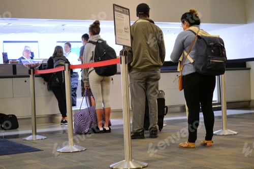 Preview: People standing in line at the ticket counter of a busy airport with their luggage and suitcases