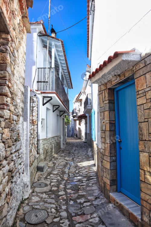 Preview: Narrow cobblestone street with blue doors and balconies in Skiathos Greece