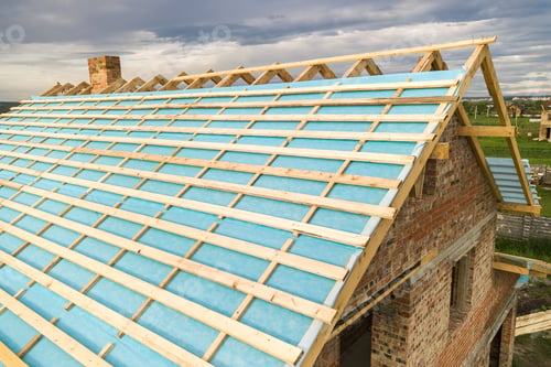 Preview: Aerial view of a brick house with wooden roof frame under construction.