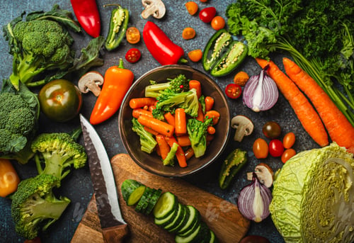 Preview: Steamed carrot broccoli salad in bowl and assorted cut fresh vegetables on rustic concrete table