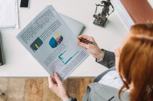 Preview: Overhead view of lawyer holding paper sheets with graphs near workplace with themis figurine on