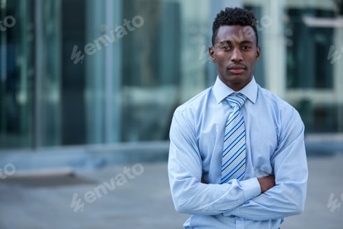 Preview: Young African American man standing by office entrance, wearing blue shirt, striped tie, copy space