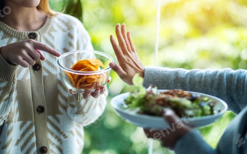 Preview: Women choosing to eat vegetables salad and making hand sign to refuse potato chips