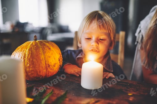 Preview: A beautiful 3-year-old boy with blonde hair sits on Halloween with a pumpkin and blows out a candle