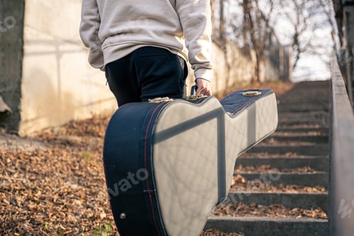 Preview: A male guitarist carries a guitar case outside.
