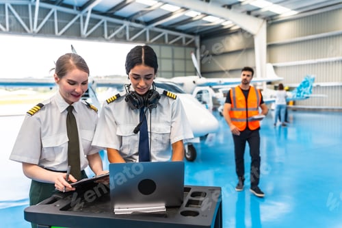 Preview: Female pilots using laptop and preparing flight plan in hangar