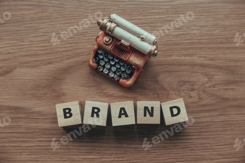 Preview: Top view of typewriter and wooden cube with text BRAND on wooden background.