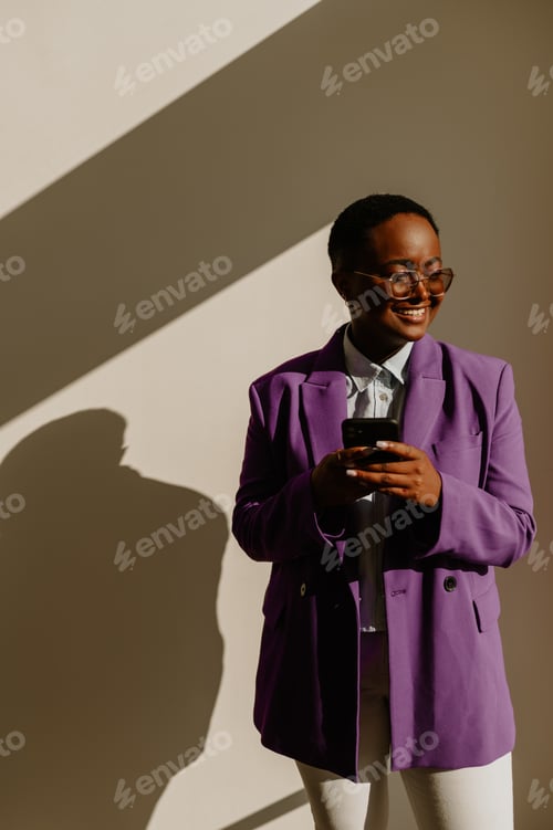 Preview: African american businesswoman using smartphone while standing over a white wall in an office