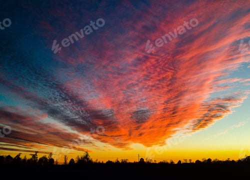 Preview: Sunset with the sun reflecting on storm clouds looks like fire in the sky with trees silhouette