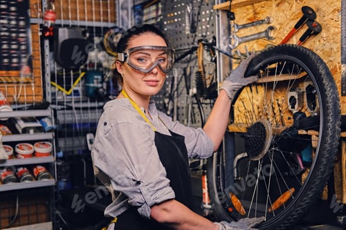 Preview: Female bicycle mechanic over tool stand background.