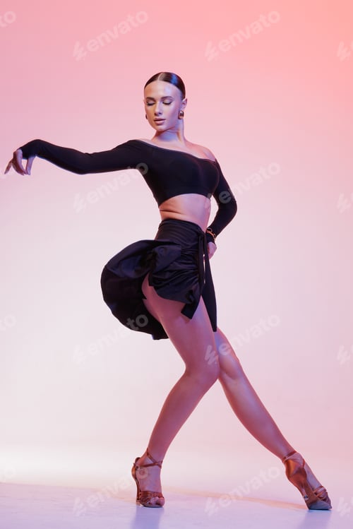 Preview: Latin dancer strikes graceful pose in black costume with skirt in motion, pink studio backdrop