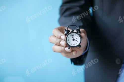 Preview: hand holding alarm clock against blue background