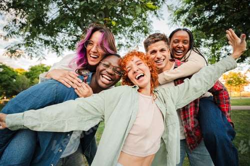 Preview: Group of joyful young friends having fun outdoors, embracing and laughing together in a park