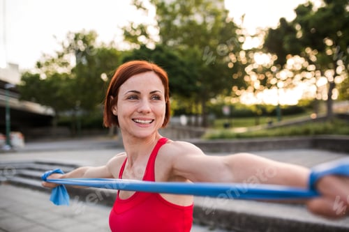 Preview: Young woman doing exercise outdoors in city with elastic bands