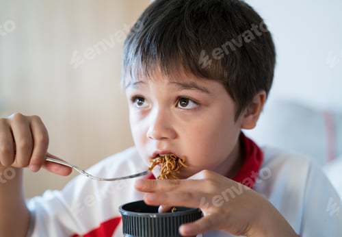 Visualização: Menino criança faminto comendo macarrão instantâneo, criança gosta de comer uma xícara de macarrão enquanto assiste TV.