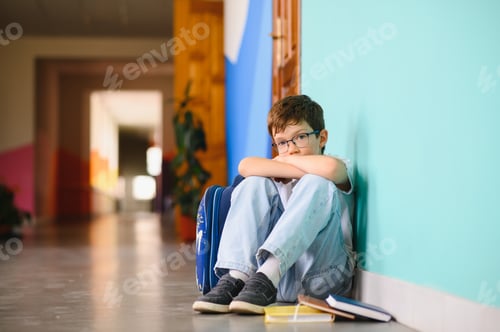 Preview: Little boy sitting alone on floor after suffering an act of bullying. Sad young schoolboy