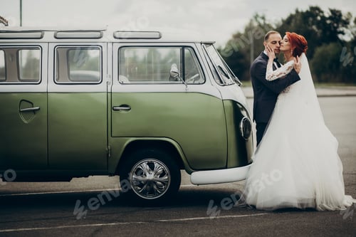 Preview: Stylish bride and groom sensually posing near retro car