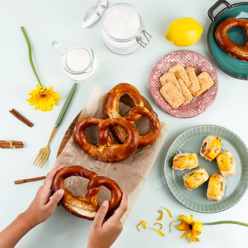 Preview: Top View Flat Lay Snacking Time with Hand, Pretzel, Biscuit, and Pastry Roll with Melted Cheese