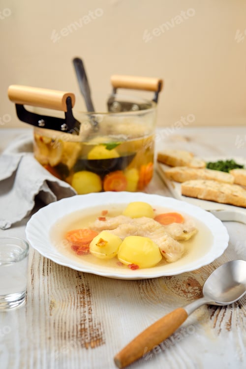Preview: Delicious homemade fish soup with vegetables served on a plate alongside crusty bread