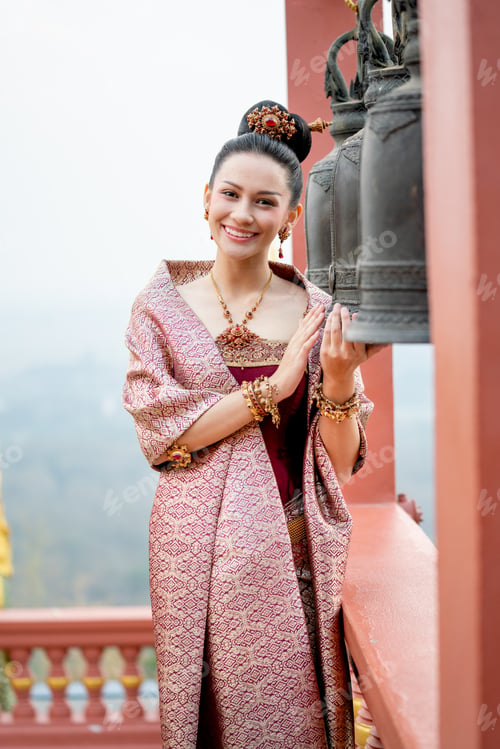Preview: Vertical image portrait of beautiful Asian woman wear Thai traditional dress stand in front of bell