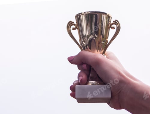 Preview: a woman holds the winner's gold cup with her hand raised to the sky