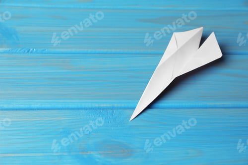 Preview: Handmade paper plane on light blue wooden table. Space for text