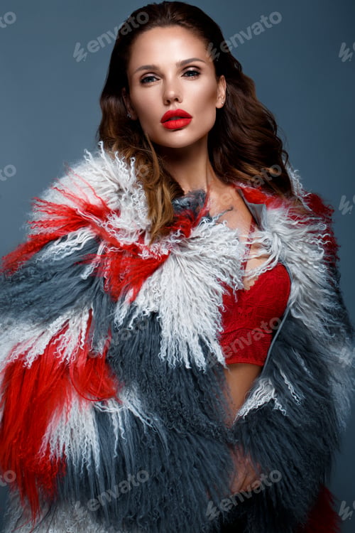 Preview: Beautiful woman with classic holiday make-up, red lips, curls in a multi-colored llama coat.
