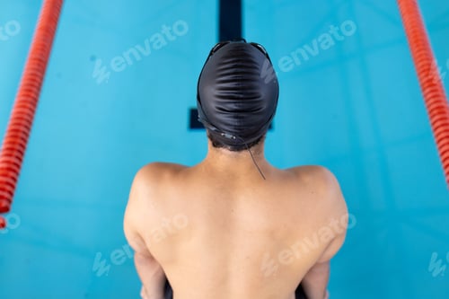 Preview: Caucasian young male swimmer standing at pool edge indoors, preparing to dive