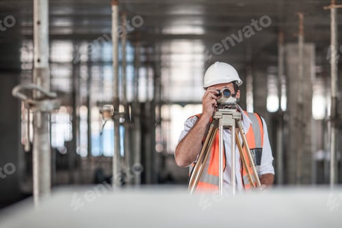 Preview: Mid adult male surveyor looking through theodolite on construction site