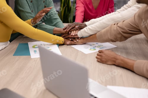 Preview: Midsection of multiracial male and female advisors stacking hands during meeting at workplace