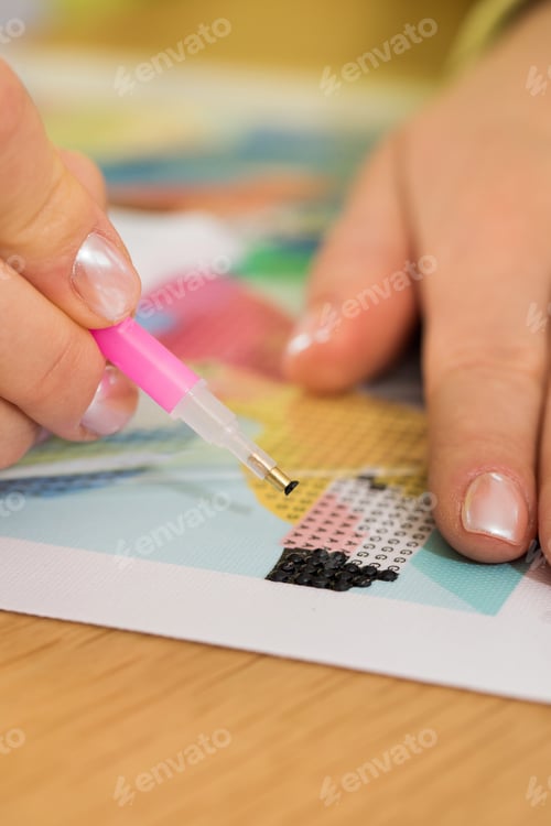 Preview: A close-up of a hand placing crystals on a canvas for a diamond painting project. Diamond Mosaic