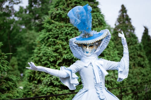 Preview: Woman in a beautiful blue carnival dress and in a venetian mask in the park on a sunny day