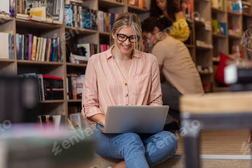 Preview: Portrait of young female student sitting at library using laptop with her friends in background.