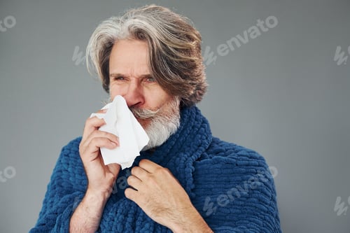 Preview: Getting sick. Against grey background. Stylish modern senior man with gray hair and beard is indoors