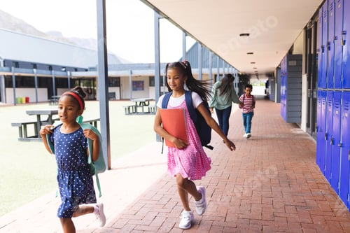 Preview: In school corridor outdoors, a biracial teacher walks behind her daughters and son, with copy space