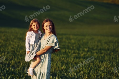 Preview: Standing and posing for a camera. Mother and daughter have fun outdoors on the field at summer