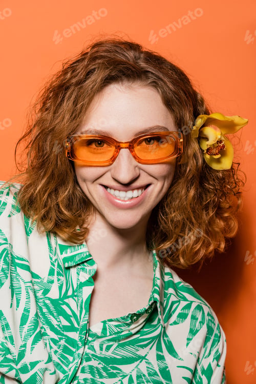Preview: Portrait of smiling and stylish young woman with orchid flower in red hair