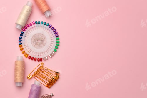Preview: Sewing accessories including thread spools and pins on pink background