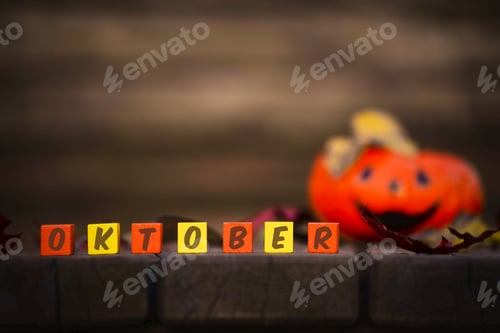 Preview: Words "October" on a Colored cubes with a laughing orange pumpkin out of focus. Halloween background
