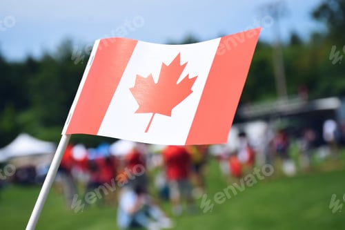 Preview: A Canadian flag with blurred fairgrounds in the background. Happy Canada Day