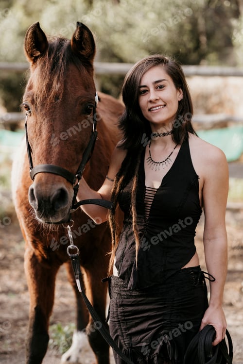 Preview: Brunette woman posing looking at the camera next to a brown horse.