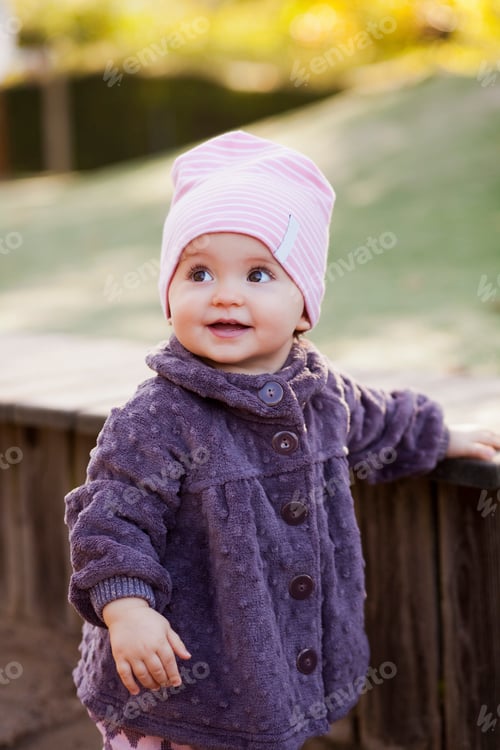 Preview: Cute baby girl standing by wooden retaining wall at park