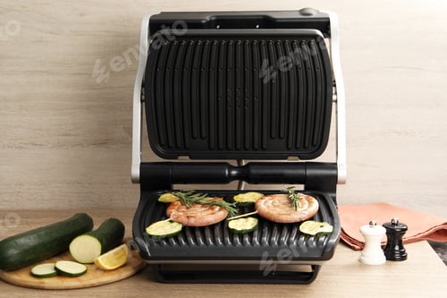 Preview: Electric grill with homemade sausages, zucchini and rosemary on wooden table
