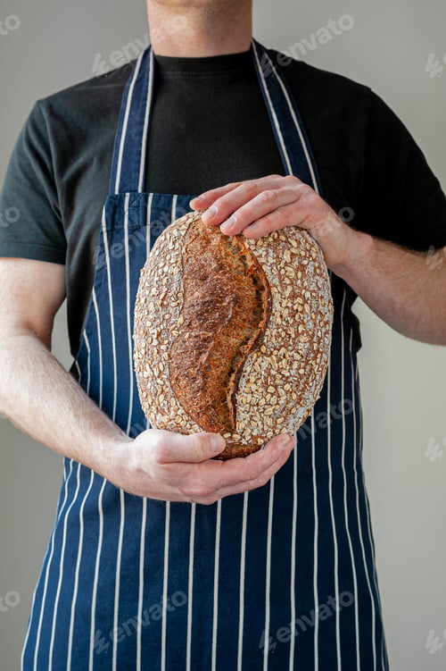 Preview: Close-up at bakers hands holding a loaf of bread in front of him.