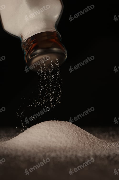 Preview: Salt is poured from a glass shaker with a metal chrome lid. Black background.